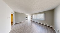 This 2-bedroom, 1-bathroom unit is laid out on a single floor, offering a straightforward and efficient floor plan. The living room is a generously proportioned space featuring light-toned laminate hardwood flooring, a textured ceiling, and a large window with vertical blinds that invites ample natural light. A baseboard heating unit runs along the exterior wall, and a wall-mounted air conditioning unit provides year-round climate comfort. A sliding glass door provides additional access and light to the living area.

The kitchen is well-equipped with white cabinetry, dark countertops, and a full suite of white appliances including an electric range, dishwasher, microwave, and refrigerator. A sink with under-cabinet lighting rounds out the functional cooking space.

Both bedrooms feature neutral carpet flooring and double-door closets with built-in hanging rods for ample storage. The primary bedroom is a comfortable, well-proportioned room with clean walls and a baseboard heater. The full bathroom includes a tub-shower combination with a clean white surround and chrome fixtures.

A connecting hallway ties all rooms together, creating a cohesive and easy-to-navigate layout. The overall aesthetic is clean and neutral throughout.