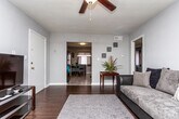 Located at 4233 Jonesboro Rd in Forest Park, Georgia, this single-floor residence offers a well-organized layout designed for comfortable everyday living. An entry hallway welcomes visitors with neutral gray walls and decorative touches, leading into the main living areas. The living room features rich hardwood-style flooring, a large sectional sofa, a plush area rug, and windows dressed with layered sheer and solid curtains that allow natural light to filter through. The kitchen is thoughtfully arranged with white cabinetry, light countertops, a black gas range, a dishwasher, and a double sink. Tile flooring runs throughout the kitchen, which also accommodates a compact dining area with a small table and seating. The primary bedroom offers carpeted flooring, multiple windows with vibrant teal and sheer curtain panels, and ample space for a full bedroom suite. A second bedroom provides a quieter, more neutral setting with soft gray tones, carpeted floors, and natural light from two windows. The bathroom features white subway tile wainscoting, a vanity with an integrated sink, a medicine cabinet mirror, and classic oil-rubbed bronze fixtures. Consistent neutral gray tones and tile and hardwood-style flooring tie the spaces together throughout.