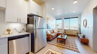 This single-floor unit showcases a thoughtfully designed open-concept layout, seamlessly connecting the kitchen, dining, and living areas. Light wood-style flooring runs throughout, creating a cohesive and airy feel across all spaces.

The kitchen is well-equipped with stainless steel appliances, including a refrigerator, electric range, built-in microwave, and dishwasher. Two-tone cabinetry — white uppers paired with gray lowers — frames granite countertops and a herringbone-patterned tile backsplash, adding a contemporary touch. A dedicated entryway with a patterned runner rug provides a welcoming transition into the home.

The living area benefits from dual large windows that frame open panoramic views, flooding the space with natural light and creating a bright, inviting atmosphere. Recessed lighting supplements throughout.

The bedroom is a calm retreat with a generously sized window offering outdoor views, white walls, and understated finishes that promote a restful environment.

The bathroom features a granite-topped vanity with gray cabinetry, a walk-in glass-enclosed shower with vertically striped tile, and wood-look flooring that ties cohesively to the rest of the unit. Overall, the space balances modern design with a warm, comfortable ambiance.
