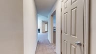 This single-story residence offers a well-organized layout connecting several distinct living spaces. The entryway opens through a six-panel door into a hallway that provides immediate sightlines into the main living area and kitchen beyond.

The living room serves as the focal point of the space, highlighted by a tile-surround fireplace with a glass-front insert. A ceiling fan with integrated lighting is centrally mounted overhead, and multiple windows fitted with horizontal blinds allow natural light to fill the room. The adjoining area extends the overall footprint, providing flexible space for dining or additional seating arrangements.

The kitchen is functionally designed with light-toned cabinetry, gray laminate countertops, and a full suite of black appliances including a range, microwave, refrigerator, and dishwasher. A double-basin sink with a modern faucet is positioned along a peninsula counter, reinforcing an open connection to the living areas. Light wood-style flooring runs throughout the kitchen.

Multiple bedrooms feature neutral carpet, ceiling fans with lighting, and windows that provide outdoor views and natural light. The bathroom includes a gray vanity with an under-mount sink, gray countertop, a large mirror with overhead bar lighting, and light wood-style flooring throughout. A textured ceiling is consistent across the entire unit.