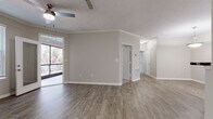 This single-floor residence offers a thoughtfully designed layout that balances open communal spaces with comfortable private quarters. The main living area makes an immediate impression with its wood-look plank flooring, neutral warm-gray walls, crown molding, and a ceiling fan overhead. Natural light filters in through a large sliding glass door that opens to a private balcony, offering views of surrounding greenery. The open-concept design connects the living space to a well-equipped kitchen, which features white cabinetry, dark countertops, stainless steel appliances including a refrigerator and microwave, and a breakfast bar that serves as a convenient dividing point between the kitchen and living areas. A hallway leads to the private bedroom spaces, each finished with plush neutral carpeting and ceiling fans. The bedrooms benefit from natural light through blinded windows. The bathroom is clean and functional, featuring tile flooring, a full soaking tub with tile surround, a vanity with white cabinetry, dark countertops, and a large mirror illuminated by overhead lighting. Throughout the residence, consistent neutral tones and cohesive finishes create a calm, move-in-ready ambiance suited for comfortable everyday living.