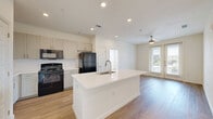 Located at 740 14th Street in Plano, TX, this well-appointed 2-bedroom, 2-bathroom residence offers a thoughtfully designed single-floor layout. The open-concept kitchen and living area serves as the heart of the home, anchored by a large white quartz island with an undermount sink — ideal for both meal prep and casual dining. The kitchen features light gray shaker-style cabinetry, a subway tile backsplash, black appliances including a gas range, built-in microwave, refrigerator, and dishwasher, along with a dedicated pantry for added storage. Warm-toned hardwood-style flooring flows throughout the entire residence, complementing the bright, neutral palette of the walls and trim. The living area extends toward French doors that lead to an outdoor space, while a ceiling fan overhead enhances comfort. The primary bedroom is generously sized, featuring a ceiling fan, large windows with outdoor views, and direct access to a well-lit bathroom with a soaking tub, white vanity, and a walk-in closet with wire shelving. The second bedroom offers equally clean finishes and ample closet space. A dedicated laundry area and multiple closets throughout add to the functional appeal of this contemporary Plano residence.