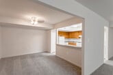 This single-floor residence offers a well-organized layout across several interconnected rooms, all finished with neutral-toned carpet and cream-colored walls that create a clean, cohesive aesthetic throughout. The living area is generously proportioned, providing ample space for furnishings, and connects openly to additional rooms via wide doorways. A pass-through window with a breakfast bar counter bridges the living space and the kitchen, enhancing the sense of openness while maintaining defined zones.

The kitchen is equipped with warm oak cabinetry, granite-style laminate countertops, a gas range with overhead ventilation, and a white refrigerator. Notably, in-unit washer and dryer units are housed within the kitchen area, offering added convenience. The bathroom features a vanity with a wood cabinet base, a wide mirror above the sink, and a full tub and shower combination surrounded by classic white tile.

The bedrooms are carpeted and well-sized, with one bedroom featuring a walk-in closet. Additional rooms include a lower-windowed space suitable for a bedroom or flexible-use room, with ceiling light fixtures providing consistent illumination. The overall layout is practical and functional, suited for comfortable everyday living.