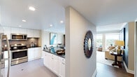 This well-designed single-floor residence offers a generous and functional layout across a thoughtfully organized floor plan. The open-concept kitchen and living area serves as the heart of the home, where white shaker-style cabinetry, dark countertops, a tile backsplash, and stainless steel appliances — including a refrigerator and dishwasher — create a clean, modern aesthetic. A built-in peninsula provides additional prep and serving space. The living room is warm and inviting, featuring hardwood-style flooring, a media console with a fireplace, and large windows that flood the space with natural light and offer elevated views of the surrounding greenery and cityscape. A dedicated office provides a quiet retreat with its own large window, carpeted flooring, and ample workspace. The spacious primary bedroom features soft carpet, direct access to a walk-in closet outfitted with custom built-in shelving, drawers, and hanging rods, as well as a connected bathroom. The bathroom includes full tile surround, a soaking tub, and tile flooring. A separate laundry room houses a stacked washer and dryer alongside a water heater, adding everyday convenience. The hallway connects all rooms seamlessly, completing this cohesive and comfortable residence.