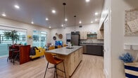 This well-appointed single-floor residence offers a thoughtfully designed open-concept layout that seamlessly connects the kitchen, dining, and living areas. The kitchen is a standout feature, anchored by a large island with a quartz-style countertop and seating for multiple guests. It is outfitted with stainless steel appliances — including a full-size refrigerator, electric range, microwave, and dishwasher — complemented by a two-tone cabinetry scheme of light wood upper cabinets and charcoal lower cabinets, along with open shelving for display.

The living area is bright and welcoming, featuring large sliding glass doors that open to an outdoor balcony, flooding the space with natural light. Light hardwood-style flooring runs throughout the entire residence, lending a clean, cohesive aesthetic.

The unit includes two well-sized bedrooms. The primary bedroom features a walk-in closet and a window for natural light, while the second bedroom offers ample space and closet access. Both bathrooms are finished consistently, each with a full tub-shower combination, a gray vanity with a quartz countertop, and light flooring. Recessed lighting throughout the residence provides consistent, modern illumination across all rooms.