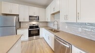 This well-appointed single-floor unit offers a thoughtfully designed open-concept layout encompassing a living room, kitchen, bedroom, bathroom, and closet. The kitchen serves as the centerpiece of the home, showcasing crisp white shaker cabinetry, warm quartz countertops, a classic subway tile backsplash, and a full suite of stainless steel appliances including a refrigerator, range, microwave, and dishwasher. A central island with pendant lighting above provides additional prep space and casual seating, while light-toned hardwood-style flooring unifies the kitchen and living areas. The living room is bright and airy, benefiting from generous natural light through a large sliding glass door that opens to a private balcony with views of the surrounding neighborhood. The bedroom is a comfortable retreat featuring plush carpet, a ceiling fan, and a sizable window that continues the theme of natural light throughout the unit. A dedicated closet provides convenient storage. The bathroom is finished to match the home's modern aesthetic, with white shaker cabinetry, quartz countertops, a single undermount sink, and a full bathtub-shower combination. In-unit laundry is also present, adding to the overall functionality of this clean, contemporary space.