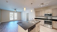 Located at 2700 E McKinney St in Denton, TX, this single-story residence offers a thoughtfully designed layout with 2 bedrooms, 2 bathrooms, and 3 closets. The open-concept kitchen serves as the heart of the home, featuring a large center island with dark granite countertops, an integrated sink, pendant lighting, light-toned cabinetry, and a full suite of stainless steel appliances including a refrigerator, range, and microwave. The kitchen flows seamlessly into the living area, which is brightened by natural light from glass French doors and outfitted with wood-look flooring and a ceiling fan. The primary bedroom is a generous retreat with its own ceiling fan, walk-in closet with built-in shelving, and a private en-suite bathroom. The en-suite bath features dark granite countertops, dual sinks, and a tiled shower. The second bedroom mirrors the home's clean, bright aesthetic with light wood flooring, a ceiling fan, and convenient closet access. Both bathrooms carry consistent, modern finishes. Wood-look flooring runs throughout the common areas, while a connecting hallway links all rooms efficiently. The overall ambiance is clean, modern, and functional, offering comfortable single-level living.