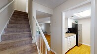 This two-floor residence offers a well-organized layout with a clear separation between living and sleeping areas. The main level features warm hardwood flooring throughout the open living and dining areas, which are bathed in natural light. The kitchen is equipped with white cabinetry, granite-style countertops, stainless steel appliances including an electric range and over-the-range microwave, and a stainless steel sink. A convenient in-unit stacked washer and dryer is tucked neatly into a closet on the main floor, alongside sliding door access to the outdoors. A full bathroom on this level includes a tub-shower combination with clean white finishes. A carpeted staircase with a white railing leads to the upper level, where multiple bedrooms feature plush wall-to-wall carpeting, ceiling fans with light fixtures, and natural light from windows. Each bedroom is generously sized and includes closet access, with at least one room offering a walk-in closet. Textured ceilings are consistent throughout the home. The neutral color palette and functional design make this a comfortable and practical living space across both floors.