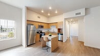 Located at 328 S Escondido Blvd in Escondido, CA, this 2-bedroom, 2-bathroom residence offers a well-designed single-floor layout with a clean, contemporary aesthetic throughout. The open-concept living and kitchen area is a standout feature, boasting soaring ceilings, light wood-look flooring, and an abundance of natural light streaming through large windows with vertical blinds. The kitchen is thoughtfully equipped with warm wood cabinetry, granite-style countertops, a central island with bar seating, and a full suite of stainless steel appliances including a refrigerator, range, microwave, and dishwasher. The living area provides a spacious, airy feel with direct access to the entry. Both bedrooms feature plush carpeting and generous windows that frame outdoor views of the surrounding neighborhood, with the primary bedroom offering sliding glass door access to a private balcony. The two bathrooms are finished with light wood-look flooring, white vanities, and tub-shower combinations with curved curtain rods. Louvered closet doors and ample storage add functional appeal throughout this well-appointed Escondido residence.