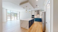 Located along Rocky Point Drive in Tampa, FL, this beautifully designed single-floor residence showcases a thoughtful blend of modern elegance and functional living. The open-concept layout is anchored by a showstopping kitchen featuring two-tone cabinetry — crisp white upper cabinets with glass-front accents and rich teal lower cabinets, all accented with gold hardware. A generous waterfall-edge quartz island serves as the centerpiece, illuminated by elegant gold pendant lights. Stainless steel appliances, a professional-grade range hood, and a deep copper sink complete this chef-inspired space. Floor-to-ceiling windows flood the living area with natural light and hint at outdoor access. The primary bathroom is a spa-like retreat, boasting a freestanding soaking tub, floor-to-ceiling marble-style tile, a dual-sink navy vanity with gold fixtures, and a separate glass-enclosed shower. Secondary bathrooms mirror the same refined aesthetic with matching teal cabinetry and marble-style tile surrounds. Bedrooms are generously proportioned with warm hardwood-style flooring and walk-in closets featuring built-in shelving systems. A dedicated in-unit laundry room with full-size washer and dryer adds everyday convenience throughout this polished Tampa residence.