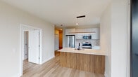 Located in Chicago's vibrant West Loop neighborhood at 1125 W Van Buren St, this contemporary single-floor residence showcases a thoughtfully designed open layout with modern finishes throughout. Light-toned hardwood floors run continuously across the living spaces, creating a warm and cohesive aesthetic.

The kitchen serves as a central focal point, featuring a peninsula with a warm wood-grain base and a crisp white quartz countertop, complemented by a built-in sink with a matte black faucet. White upper cabinetry extends to the ceiling, while stainless steel appliances — including a gas range, microwave, and French door refrigerator — complete the culinary space. A sleek linear pendant light anchors the kitchen visually.

The living and bedroom areas benefit from dramatic floor-to-ceiling windows with black framing, flooding the interior with natural light and offering sweeping views of the Chicago cityscape, including surrounding rooftops and urban landmarks. The clean, neutral wall tones enhance the brightness throughout.

The bathrooms are finished with striking marble-look tile flooring and floating vanities with light wood cabinetry, large rectangular mirrors, and glass-enclosed shower enclosures. Recessed lighting provides even illumination throughout the unit, reinforcing the clean, contemporary character of this well-appointed Chicago residence.