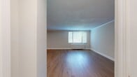 This 850-square-foot, one-bedroom, one-bathroom apartment is thoughtfully laid out across a single floor, offering an efficient and modern living environment. The living room is bright and open, featuring warm hardwood flooring, crown molding, a textured ceiling, and large windows with blinds that invite natural light and outdoor views of surrounding trees. The galley-style kitchen is well-appointed with two-tone cabinetry — warm wood lower cabinets paired with white upper cabinets — complemented by white quartz countertops and stainless steel appliances including a gas range, refrigerator, and microwave. The primary bedroom spans 230 square feet and includes hardwood floors, a dedicated closet with built-in shelving, and a window offering natural light. Neutral gray walls and recessed lighting throughout the unit contribute to a clean, contemporary aesthetic. The bathroom features a wood-toned vanity with a white countertop, a mirrored medicine cabinet, and brushed nickel fixtures. A dedicated laundry area houses a stacked washer and dryer unit alongside an electrical panel, maximizing utility within the floor plan. The consistent use of light hardwood flooring throughout unifies the space and enhances its airy, modern feel.
