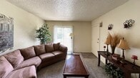 Located at 7643 E 51st St in Tulsa, Oklahoma, this single-story unit offers a well-organized, functional layout across a comfortable footprint. The living room serves as the central gathering space, featuring neutral-toned walls, textured popcorn ceilings, and plush carpeted flooring throughout. A sliding glass door fitted with vertical blinds allows natural light to filter in and provides access to an outdoor area, contributing to an open and airy feel. The living room is generously sized to accommodate a full sectional arrangement with room to spare.

The two bedrooms continue the warm, neutral palette, each featuring carpeted floors, textured ceilings, and windows dressed with blinds and curtains that allow for natural light control. The bedrooms offer adequate space for standard furniture arrangements including full or queen-sized beds and additional storage pieces.

The unit includes two bathrooms, each with a vanity featuring wood cabinetry, a single basin sink with a countertop surround, and a shower-tub combination enclosed by a curtain. Dark tile flooring is present in one bathroom, adding a contrasting visual element. Both bathrooms are practical and well-appointed for daily use.

Overall, this Tulsa property presents a straightforward, livable space with consistent finishes and a cohesive, understated aesthetic throughout.