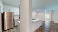 Located at 22743 Preakness Blvd in Land O' Lakes, Florida, this single-floor residence offers a well-designed layout with a clean, modern aesthetic throughout. The open-concept living and dining area is anchored by rich wood-look flooring and a ceiling fan with a light fixture, creating a bright and airy atmosphere. A sliding glass door with vertical blinds fills the living space with natural light and provides outdoor access. The kitchen is a standout feature, showcasing crisp white cabinetry, a large white quartz peninsula with a deep double-basin sink and a high-arc chrome faucet, and stainless steel appliances including a refrigerator, range, and microwave. Recessed and overhead lighting keeps the kitchen well-illuminated. The bedrooms are generously proportioned, finished with plush neutral carpeting, and offer ample natural light through large windows with views of surrounding greenery. Each bedroom includes dedicated closet space, with at least one featuring a walk-in closet with built-in shelving. Both bathrooms are finished consistently, featuring white cabinetry with quartz countertops, a large mirror, and a tub-shower combination, all set atop wood-look tile flooring. The overall design maintains a neutral, cohesive palette with white walls and chrome fixtures throughout, lending the space a fresh and move-in-ready feel.