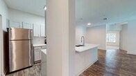 Located at 22743 Preakness Blvd in Land O' Lakes, Florida, this single-floor residence offers a well-designed layout with a clean, modern aesthetic throughout. The open-concept living and dining area is anchored by rich wood-look flooring and a ceiling fan with a light fixture, creating a bright and airy atmosphere. A sliding glass door with vertical blinds fills the living space with natural light and provides outdoor access. The kitchen is a standout feature, showcasing crisp white cabinetry, a large white quartz peninsula with a deep double-basin sink and a high-arc chrome faucet, and stainless steel appliances including a refrigerator, range, and microwave. Recessed and overhead lighting keeps the kitchen well-illuminated. The bedrooms are generously proportioned, finished with plush neutral carpeting, and offer ample natural light through large windows with views of surrounding greenery. Each bedroom includes dedicated closet space, with at least one featuring a walk-in closet with built-in shelving. Both bathrooms are finished consistently, featuring white cabinetry with quartz countertops, a large mirror, and a tub-shower combination, all set atop wood-look tile flooring. The overall design maintains a neutral, cohesive palette with white walls and chrome fixtures throughout, lending the space a fresh and move-in-ready feel.