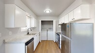 This single-floor, 2-bedroom, 1-bathroom home offers a practical and comfortable layout designed to make efficient use of its space. Light gray walls, light wood-toned flooring, and textured ceilings are consistent throughout, creating a cohesive and clean aesthetic.

The open living and dining area is bright and airy, anchored by sliding glass doors that invite natural light and provide access to an outdoor area with a fenced yard. The space flows naturally into the galley-style kitchen, which features white cabinetry with ample storage, light stone-look countertops, a matte black faucet with a single-basin sink, and a full suite of stainless steel appliances including a dishwasher, range, and refrigerator. A dedicated laundry nook within the kitchen houses a side-by-side washer and dryer, adding everyday convenience.

Both bedrooms are well-proportioned with generous closet space, including built-in closets with sliding doors. Each room benefits from natural light through sizeable windows. The primary bedroom offers a wider footprint with an outdoor-facing window view.

The full bathroom is cleanly appointed with a single-sink vanity, a tub-shower combo, and a window above the tub for natural ventilation and light. Three closets throughout the home provide ample storage to complement this efficiently organized floor plan.
