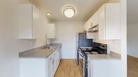 This 2-bedroom, 1-bathroom single-floor unit offers a clean, functional layout with a cohesive design throughout. Light wood laminate flooring runs continuously across all rooms, creating a warm and unified aesthetic against the crisp white walls and trim.

The open living area connects directly to the galley-style kitchen, which is well-appointed with white shaker cabinetry, gray laminate countertops, a stainless steel sink, and stainless steel appliances including an electric range and refrigerator. Overhead flush-mount lighting brightens the kitchen, which also benefits from an open-concept connection to the main living space. A ceiling fan with a light fixture adds comfort to the living area.

The primary bedroom is a comfortable size and features a window with blinds that draws in natural light and offers views of surrounding greenery. The second bedroom is also well-proportioned and includes its own window, providing ventilation and additional natural light. Both bedrooms feature baseboard heating units. The bathroom is neatly finished with white cabinetry, a gray countertop vanity, a wall-mounted mirror, and matching brushed nickel hardware. A hallway connects the bedrooms and bathroom, providing a practical flow throughout the unit.