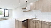 This thoughtfully designed two-bedroom, one-bathroom unit on N Sixth St in Newark, NJ, offers a cohesive modern aesthetic throughout its single-floor layout. Light-toned hardwood flooring flows continuously across the space, complementing the bright, neutral walls that create a clean and airy atmosphere.

The kitchen is a standout feature, showcasing light wood-grain cabinetry paired with crisp white quartz countertops and a textured white subway tile backsplash. A peninsula with built-in dishwasher adds functional workspace, while cylindrical pendant lights provide focused illumination. Stainless steel appliances, including a refrigerator, range, and microwave, complete the well-equipped space. Floating shelves add additional storage options.

The bedrooms are finished with the same light hardwood flooring and feature generous natural light through large windows. The primary bedroom includes dual closets with dedicated shelving and hanging space, offering practical storage solutions.

The bathroom is finished with large-format tile flooring and marble-style wall tile surrounding the full soaking tub and shower. A wood-toned floating vanity with a white countertop, round mirror, and modern light fixture complete the polished look throughout.