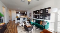 This single-floor residence offers a thoughtfully designed open-concept layout that seamlessly connects the living area and kitchen, creating a cohesive and functional living space. The living room is a standout area, featuring rich hardwood-style flooring, a ceiling fan, and an abundance of natural light filtering through large windows with horizontal blinds. A bold gallery wall of black-framed abstract artwork serves as a striking focal point, complementing the contemporary aesthetic of the space.

The kitchen is well-equipped with dark espresso cabinetry, stainless steel appliances including a refrigerator with ice maker, range, and built-in microwave, as well as light quartz countertops and a subway tile backsplash. A peninsula with bar seating and pendant lighting provides additional dining and prep space, while recessed lighting enhances the functional layout. A hallway with wood-style flooring connects the main living area to additional rooms, offering storage closets along the way.

The bedroom is comfortably sized with a window that welcomes natural light and is finished with neutral tones and plush carpeting. The bathroom features dark cabinetry, a light countertop, tile flooring, and a tub-shower combination, with direct access to a walk-in closet, providing practical everyday convenience.