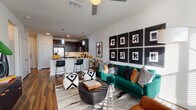 This single-floor residence offers a thoughtfully designed open-concept layout that seamlessly connects the living area and kitchen, creating a cohesive and functional living space. The living room is a standout area, featuring rich hardwood-style flooring, a ceiling fan, and an abundance of natural light filtering through large windows with horizontal blinds. A bold gallery wall of black-framed abstract artwork serves as a striking focal point, complementing the contemporary aesthetic of the space.

The kitchen is well-equipped with dark espresso cabinetry, stainless steel appliances including a refrigerator with ice maker, range, and built-in microwave, as well as light quartz countertops and a subway tile backsplash. A peninsula with bar seating and pendant lighting provides additional dining and prep space, while recessed lighting enhances the functional layout. A hallway with wood-style flooring connects the main living area to additional rooms, offering storage closets along the way.

The bedroom is comfortably sized with a window that welcomes natural light and is finished with neutral tones and plush carpeting. The bathroom features dark cabinetry, a light countertop, tile flooring, and a tub-shower combination, with direct access to a walk-in closet, providing practical everyday convenience.