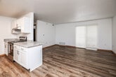 This single-floor residence offers a clean, modern aesthetic with consistent light wood-tone flooring running throughout every room. The open-concept layout connects the kitchen directly to the living area, creating a spacious and functional common space. The kitchen is well-equipped with white shaker-style cabinetry, granite-look countertops, stainless steel appliances including a refrigerator, range, and dishwasher, and a double-basin sink. A peninsula provides additional prep space and helps define the boundary between the kitchen and living area. The living room receives natural light through a large sliding glass door fitted with blinds. The bedrooms are generously sized, each featuring wood-look flooring, textured ceilings, warm wood baseboards, and windows with blinds that allow for adjustable natural light. The space includes two bathrooms: one full bath with a tub-shower combination, white vanity, and wood-framed mirror, and a second bathroom featuring a white vanity with a large mirror and towel bars. A dedicated laundry area houses a full-sized top-load washer and dryer with overhead wire shelving. Throughout the space, neutral wall tones and consistent finishes create a cohesive, move-in-ready environment.