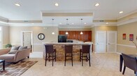 Located along Chapel Lakes Loop in Wetumpka, Alabama, this single-floor space offers a thoughtfully designed layout with distinct functional areas connected by consistent architectural detailing throughout. Crown molding, chair rail wainscoting, and tray ceilings are recurring elements that lend a refined, cohesive character to the interior.

The kitchen serves as a central focal point, showcasing a generously sized curved island clad in stacked stone with a light countertop surface and seating for multiple bar stools. Rich cherry-toned cabinetry lines the perimeter walls alongside a black refrigerator and microwave. Three pendant lights hang above the island, complementing the recessed lighting overhead. Large-format tile flooring extends through the kitchen and into adjoining areas.

The main living area features a tray ceiling with a ceiling fan, a stacked stone fireplace with a white mantle, and multiple windows allowing natural light to filter in. Adjacent to this is a more casual lounge space with warm hardwood flooring, additional seating, and natural light from multiple windows.

The dining area benefits from a tray ceiling, large windows overlooking outdoor surroundings, and a built-in buffet with matching cherry cabinetry. A dedicated built-in sideboard area with upper and lower cabinetry provides additional storage nearby. The overall ambiance is warm, elegant, and well-suited for both gathering and everyday use.