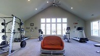 Located at 5315 Avery Road in Dublin, Ohio, this fitness center offers a welcoming and functional environment for exercise and wellness. The space is defined by its impressive vaulted ceiling, which rises dramatically overhead and is complemented by a large ceiling fan that ensures comfortable air circulation throughout workouts. Recessed lighting is evenly distributed across the ceiling, providing consistent illumination throughout the space.

A striking bank of tall, multi-pane windows dominates one wall, flooding the interior with natural light and offering views of the surrounding outdoor environment. The bright, airy ambiance created by this generous fenestration makes the space feel open and energizing.

The fitness area is equipped with a range of cardio machines, including treadmills, an elliptical trainer, and a stationary bike, all thoughtfully arranged to allow ample room for movement. A cushioned seating piece provides a comfortable spot to rest between sets. Framed artwork and motivational décor adorn the walls, adding a personalized touch to the environment. Soft, patterned carpeting covers the floor, contributing to the overall comfort of the space. The single-floor layout ensures easy accessibility, making this a practical and inviting fitness destination.