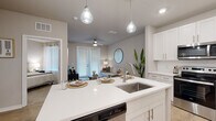 This thoughtfully designed single-floor residence showcases a bright, open-concept layout that seamlessly connects the kitchen and living areas. The kitchen is a standout feature, equipped with full-height white shaker cabinets, stainless steel appliances including a range, microwave, and French door refrigerator, and a large center island with a white quartz countertop, undermount sink, and bar seating for two. Pendant lighting adds a stylish touch overhead, while light wood-style flooring ties the space together.

The living area is airy and welcoming, benefiting from natural light through French doors fitted with horizontal blinds. A ceiling fan enhances comfort, and the neutral gray walls provide a versatile backdrop for any décor style.

The bedroom offers a serene retreat with plush carpet, ample natural light from a double-pane window, and soft, neutral tones that create a calm atmosphere. The bathroom is generously proportioned, featuring a wide dual-sink vanity with a quartz countertop, a framed mirror, and a glass-enclosed walk-in shower with large-format tile surround. Wood-style flooring extends throughout the bathroom, reinforcing the cohesive, modern aesthetic found across the entire residence.
