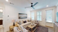 This single-story unit in Santa Rosa Beach, Florida, offers a thoughtfully designed coastal retreat with modern finishes and a cohesive, neutral aesthetic throughout. The living room serves as the centerpiece of the home, featuring white walls, crown molding, and a striking blue-bladed ceiling fan that adds a nautical touch. Multiple windows fitted with plantation-style blinds fill the space with natural light, while hardwood-style flooring and a patterned area rug add warmth and texture. A large coastal landscape painting anchors the main wall, complementing the relaxed, beach-inspired décor.

The kitchen is outfitted with dark wood cabinetry, white quartz countertops, and a full suite of stainless steel appliances, including a side-by-side refrigerator, range, and microwave. Light wood-style flooring carries through to a dedicated laundry area accessible directly from the kitchen.

The bedroom is a calm, well-lit retreat with light hardwood floors, recessed lighting, and a window offering natural light. It connects to a spacious walk-in closet with wire shelving for ample storage.

The bathroom features porcelain tile flooring, a glass-enclosed walk-in shower with full tile surround, and a modern vanity with a white countertop—delivering a clean, spa-like finish.