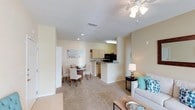 Located at 1047 Hwy 31 in Spanish Fort, Alabama, this single-floor residence offers a thoughtfully designed open-concept layout that seamlessly connects the living, dining, and kitchen areas into one cohesive and functional space. The living area is warm and inviting, featuring plush wall-to-wall carpeting and a ceiling fan with integrated lighting that provides both comfort and illumination. Neutral-toned walls throughout lend a clean, airy feel to the interior. The dining area sits adjacent to the living space, providing a defined yet open area for meals and gatherings. The kitchen is positioned at the heart of the home, anchored by a peninsula-style counter that doubles as a casual bar or prep surface. Light-toned cabinetry lines the kitchen walls, complemented by black appliances including a microwave and refrigerator. Recessed lighting in the kitchen ensures the space is well-lit and functional. Visible storage solutions, including a large white closet or pantry door near the entry, add to the practicality of the layout. The overall ambiance is bright, clean, and welcoming, with a consistent design palette of soft neutrals that makes the space feel open and easy to personalize.