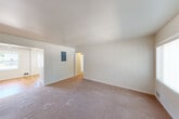 Located on Seward Park Ave S in Seattle, WA, this 2-bedroom, 1-bathroom single-floor home offers a practical and comfortable layout. The open living room is carpeted and bathed in natural light from a large window with vertical blinds, creating a bright and welcoming atmosphere. It connects seamlessly to the kitchen via a hardwood-floored entryway area. The kitchen is well-appointed with light wood cabinetry, dark countertops, black appliances including a range, over-the-range microwave, and refrigerator, plus a double sink and overhead fluorescent lighting. The primary bedroom is generously sized with carpet flooring and a window overlooking the outdoors. The secondary bedroom features warm hardwood floors, a window, and track lighting overhead. The bathroom includes a wood-cabinet vanity with a mirrored medicine cabinet and overhead lighting. A dedicated laundry room houses a stacked Whirlpool washer and dryer unit alongside built-in shelving. Four closets throughout the home provide excellent storage. A connecting hallway ties all rooms together efficiently. The space maintains a clean, neutral palette throughout, offering a move-in-ready canvas.