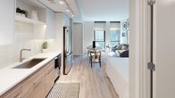 Located at 33 N St NE in Washington, DC, this single-floor residence showcases a clean, contemporary design with a cohesive palette of light wood, white, and neutral tones throughout. The open-concept living area flows seamlessly from the kitchen to the dining and living spaces, all anchored by light-toned hardwood flooring. Large floor-to-ceiling windows in the living area flood the space with natural light and frame views of the surrounding neighborhood, creating an airy, inviting atmosphere. The kitchen is thoughtfully appointed with two-tone cabinetry — white upper cabinets paired with warm wood-finish lower cabinets — complemented by white quartz countertops, a classic subway tile backsplash, stainless steel GE appliances including a range, microwave, and refrigerator, and an undermount sink. A dedicated dining area with a round table sits between the kitchen and living space, optimizing the open floor plan. The bedroom is a calm retreat with soft gray walls, light hardwood floors, curated wall art, and access to a walk-in closet. The bathroom features large-format earth-toned tile flooring, a wood-finish vanity with a white countertop, and a glass-enclosed shower, completing this well-designed urban residence.