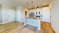 Located at 4700 Wagon Rd in Santa Fe, NM, this single-story one-bedroom, one-bathroom home offers a thoughtfully designed layout with modern finishes throughout. Light-toned hardwood-style flooring runs through the main living areas, complementing the neutral gray walls and clean white trim that give the space a bright, cohesive feel. The open-concept kitchen serves as the heart of the home, featuring a central island with pendant lighting overhead, crisp white cabinetry, stone countertops, and a full suite of stainless steel appliances including a refrigerator, electric range, and over-the-range microwave. The living area flows naturally from the kitchen, with natural light entering through blinds-fitted windows. The bedroom is carpeted for comfort, benefits from multiple windows, and includes a ceiling fan. A dedicated closet provides organized storage. The bathroom is well-appointed with white vanity cabinetry, a stone countertop, a full tub-shower combination with floor-to-ceiling tile surround, and consistent hardwood-style flooring. A separate laundry room houses a full-size top-loading washer and dryer, adding everyday convenience. The overall design balances function and modern simplicity, making this Santa Fe home practical and move-in ready.