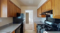 Princeton Gardens, Unit 204 is a single-floor residence that offers a practical and comfortable layout across several well-defined living spaces. The galley-style kitchen is efficiently organized, featuring warm wood cabinetry on both sides, granite-look countertops, and a full suite of black appliances including a gas range, refrigerator, and dishwasher. A range hood is positioned above the stove, and the kitchen opens directly into the adjoining living areas for easy flow.

The living room is generously proportioned, with plush wall-to-wall carpeting, neutral-toned walls, and a sliding glass door dressed with vertical blinds that invites natural light and provides outdoor access. Baseboard heating runs along the perimeter, ensuring consistent warmth throughout. A wall-mounted air conditioning unit is also present for year-round climate control.

The dining area is a dedicated space illuminated by a classic chandelier and a window with blinds that brings in additional natural light. It sits adjacent to the kitchen, making it convenient for everyday dining.

The bedroom features carpeted flooring, a bright window with a view of surrounding greenery, and baseboard heating. The bathroom includes tile flooring, a soaking tub with tiled surround, and warm wood vanity cabinetry with a granite-look countertop.