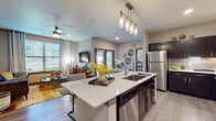 This well-appointed single-floor residence offers a thoughtfully designed open-concept layout that seamlessly connects the kitchen, dining, and living areas. The kitchen is a standout feature, showcasing dark espresso cabinetry with brushed hardware, white quartz countertops, a large center island with an undermount sink, stainless steel appliances, and elegant pendant lighting overhead. Wood-look flooring flows throughout the main living spaces, adding warmth and cohesion to the design.

The living room is bright and inviting, benefiting from large windows that bring in generous natural light and views of the surrounding greenery. A ceiling fan adds comfort, while the open connection to the kitchen and dining area makes the space ideal for everyday living. The dedicated dining nook features a marble-top round table beneath a window with outdoor views, creating a pleasant setting for meals.

Both bedrooms are comfortably sized with plush carpeting, large windows, and ample closet space. The primary bathroom features a dual-sink vanity with quartz countertops and a walk-in closet, while the secondary bathroom offers a tiled tub-shower combination. Throughout the residence, neutral tones and contemporary finishes create a cohesive and modern aesthetic.