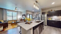 This well-appointed single-floor residence offers a thoughtfully designed open-concept layout that seamlessly connects the kitchen, dining, and living areas. The kitchen is a standout feature, showcasing dark espresso cabinetry with brushed hardware, white quartz countertops, a large center island with an undermount sink, stainless steel appliances, and elegant pendant lighting overhead. Wood-look flooring flows throughout the main living spaces, adding warmth and cohesion to the design.

The living room is bright and inviting, benefiting from large windows that bring in generous natural light and views of the surrounding greenery. A ceiling fan adds comfort, while the open connection to the kitchen and dining area makes the space ideal for everyday living. The dedicated dining nook features a marble-top round table beneath a window with outdoor views, creating a pleasant setting for meals.

Both bedrooms are comfortably sized with plush carpeting, large windows, and ample closet space. The primary bathroom features a dual-sink vanity with quartz countertops and a walk-in closet, while the secondary bathroom offers a tiled tub-shower combination. Throughout the residence, neutral tones and contemporary finishes create a cohesive and modern aesthetic.