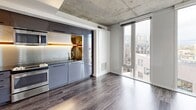 Located at 22 NE 2nd Ave in Portland, OR, this compact yet efficiently designed one-bedroom, one-bathroom unit showcases a modern urban aesthetic throughout. A clean, well-lit entrance hallway with smooth white walls and dark hardwood-style flooring leads into the main living area, with an in-unit laundry conveniently accessible along the way.

The open-concept living, dining, and kitchen area is the architectural centerpiece of the unit. Exposed concrete ceilings lend an industrial character, while floor-to-ceiling windows flood the space with natural light and offer elevated views of the surrounding Portland cityscape. The sleek kitchen features dark cabinetry with a metallic backsplash, stainless steel appliances including an oven and microwave, and a modern sink — all seamlessly integrated into the living space.

The bedroom is a comfortable and well-proportioned retreat, finished with plush carpet flooring and large sliding closet doors that maximize storage. A dedicated closet room further adds to the unit's practical storage options.

The bathroom is finished in a contemporary style with dark cabinetry, a black sink basin, a warm wood floating shelf, and a grab bar — combining functionality with clean, minimal design. The overall ambiance of the unit is sleek, modern, and efficiently organized, well-suited for urban living in Portland's vibrant Lower Burnside district.