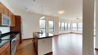 This well-appointed single-floor residence offers a thoughtfully designed open-concept layout that seamlessly connects the kitchen, dining, and living areas. The kitchen is a standout feature, showcasing rich warm-toned cabinetry, dark granite countertops, a center island with a built-in sink, and a full suite of stainless steel appliances including a range, microwave, and refrigerator. Track and pendant lighting illuminate the space with a modern touch. Durable hardwood flooring flows throughout the main living areas, complemented by crisp white walls and warm wood baseboards.

The expansive living area is bathed in natural light from large windows that frame views of the surrounding mixed-use neighborhood and lush tree canopies. A ceiling fan adds practical comfort to this generous space. Sliding glass doors open onto a private balcony, offering elevated outdoor views of the vibrant community below.

The bedrooms are carpeted and well-lit, each featuring large windows with neighborhood views and ceiling fans. The primary bathroom includes a glass-enclosed walk-in shower, a wide vanity with granite countertops, warm wood cabinetry, and tile flooring, while the secondary bathroom offers a full tub-shower combo with a similarly appointed vanity.