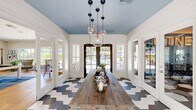 Located at 1164 E Perrin Ave in Fresno, CA, this thoughtfully designed single-floor community clubhouse offers a welcoming and versatile gathering space. The entry and dining area sets an immediate design tone with striking geometric hexagonal tile flooring in blue and white, shiplap-clad walls, a powder-blue ceiling, and a cluster of globe pendant lights suspended above a rustic wood communal table. Glazed French doors open directly to an outdoor pool area, flooding the space with natural light and seamless indoor-outdoor connectivity. The living room features vaulted ceilings, wide-plank hardwood flooring, and large windows framing lush greenery. A pool table anchors the room alongside eclectic mid-century-style seating, a wall-mounted television, and built-in banquette seating — ideal for both relaxed lounging and social interaction. A dedicated office area with shiplap accent walls, vaulted ceilings, and a substantial dark wood desk provides a functional workspace. The fitness center is a standout amenity, split across two areas: one side offers cardio machines and strength equipment on bold geometric patterned flooring, while the other showcases a vibrant blue accent wall, a full dumbbell rack, medicine balls, a punching bag, and a large illuminated "FITNESS" marquee sign with floor-to-ceiling mirrors.