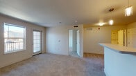 This single-floor unit offers a thoughtfully designed open-concept layout that seamlessly connects the main living areas. The living room is generously sized, featuring neutral-toned carpet, smooth walls, and a door leading to a private balcony that brings in natural light and exterior views of the surrounding community. An adjacent window further enhances the brightness of the space.

The kitchen is a standout feature, equipped with dark espresso cabinetry, black appliances including a refrigerator, range, and built-in microwave, and light countertops that provide pleasing contrast. A breakfast bar peninsula separates the kitchen from the living area, creating a natural flow between spaces. The flooring transitions to durable wood-look vinyl in the kitchen, adding warmth and practicality.

The bedrooms are carpeted and well-proportioned, offering a calm, neutral environment. One bedroom includes access to a utility area with laundry hookups, adding everyday convenience. The bathroom is clean and functional, featuring dark vanity cabinetry with ample storage, a white countertop with an undermount sink, a large mirror, and wood-look vinyl flooring. A towel bar and toilet complete the well-organized layout. Overall, the unit presents a cohesive, move-in-ready aesthetic throughout.