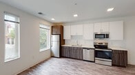 This single-floor unit showcases a clean, contemporary design throughout its well-organized layout. The kitchen is a standout feature, equipped with a full suite of stainless steel appliances including a refrigerator, electric range, built-in microwave, and dishwasher. Cabinetry combines crisp white upper cabinets with wood-grain lower cabinets in a dark walnut-style finish, complemented by light countertops and a single-basin sink. Recessed lighting and multiple windows allow natural light to fill the kitchen and adjacent living area, with views of surrounding greenery enhancing the bright, open atmosphere. Wood-style luxury vinyl plank flooring extends through the kitchen and main living spaces, providing a cohesive and durable surface. The bedroom areas offer a quieter retreat, one featuring carpet flooring and another with the same wood-style planks, each with windows that bring in natural light. The bathroom is designed with a clean, minimalist aesthetic, featuring a wide white vanity with an undermount sink, a large mirror, and wood-look tile flooring. Grab bars and accessible fixtures reflect thoughtful, functional design. Throughout the unit, neutral white walls and consistent finishes create a bright, move-in ready environment.