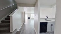 This two-story home offers a practical and modern layout across two well-proportioned floors. The main level features an open kitchen and living room area with luxury vinyl plank flooring in a cool gray tone, providing a clean, contemporary look throughout. The kitchen is equipped with white shaker-style cabinetry accented by matte black hardware, light marble-look countertops, and black appliances including a refrigerator, range, and dishwasher. A dedicated laundry room on the main floor includes overhead cabinetry, washer/dryer hookups, and a window for natural light. A half bathroom on the main level features a round mirror, matte black fixtures, and a white quartz vanity top. The living room is bright and open, with large windows allowing ample natural light and a textured ceiling overhead. Upstairs, two bedrooms are finished with plush carpet and ceiling fans, each with dedicated closet space. The primary bedroom is a comfortable size and features its own walk-in closet. Two full bathrooms on the upper level are finished with gray cabinetry, white quartz countertops, round mirrors, matte black fixtures and hardware, and tiled tub-shower surrounds. Three hallways guide the flow between spaces on both levels, and a carpeted staircase connects the floors.
