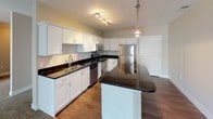 This single-floor residence at 19707 Center Ridge Rd in Rocky River, Ohio offers a well-appointed layout designed for comfortable everyday living. The kitchen serves as a central highlight, featuring crisp white shaker cabinetry, dark granite countertops, and a full suite of stainless steel appliances including a refrigerator, range, microwave, and dishwasher. A center island with matching granite provides additional prep space and casual seating, while pendant lighting and track lighting above enhance the functional aesthetic. Hardwood-style flooring runs throughout the kitchen and dining area, creating a clean transition into the open living space.

The spacious living room is carpeted and bathed in natural light through large sliding glass doors dressed with vertical blinds, offering outdoor views and easy access to a balcony or patio area. Crown molding and track lighting add refined detail to the room.

The bedrooms are quietly situated, each featuring plush carpeting, neutral wall tones, and windows with blinds that allow for natural light. The primary bathroom includes a dual-sink vanity with dark granite countertops, white cabinetry, and a glass-enclosed walk-in shower. A second full bathroom mirrors the same design language with a single-sink vanity and a tub-shower combination, finished with tile flooring throughout.