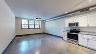 This thoughtfully designed one-bedroom, one-bathroom unit offers an open, industrial-modern aesthetic across a single floor. Polished concrete floors run throughout the entire space, providing a sleek, low-maintenance foundation that ties every room together cohesively.

The open-concept living, dining, and kitchen area is the heart of the unit. Large black-framed windows flood the space with natural light and offer street-level views, while an exposed metallic HVAC duct runs along the ceiling, reinforcing the industrial character. A ceiling fan adds comfort to the spacious living area. The kitchen features white shaker-style cabinetry, granite-look countertops, and a full suite of stainless steel appliances including a range, microwave, refrigerator, and dishwasher.

A long hallway connects the main living area to the private quarters, lined with polished concrete floors and overhead lighting. The bedroom is generously sized, includes a ceiling fan, and is served by natural light through a horizontal window with roller shade. Two closets provide ample storage, one of which features wire shelving systems for organized use.

The bathroom showcases white subway tile surrounding a soaking tub and tub surround, accented with matte black fixtures for a crisp, contemporary contrast. An in-unit laundry area completes this well-appointed, urban-inspired space.