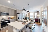 Located at 1950 Winrock Blvd in Houston, TX, this well-appointed 2-bedroom, 2-bathroom residence offers a thoughtfully designed single-level layout. The open-concept living, dining, and kitchen area serves as the heart of the home, bathed in natural light from large windows and a glass balcony door. The kitchen is a standout feature, showcasing gray shaker-style cabinetry, a white quartz waterfall island with bar seating, stainless steel appliances, and stylish pendant lighting — ideal for both cooking and entertaining. Hardwood-style flooring flows throughout the space, adding warmth and continuity. The living area connects seamlessly to the outdoor balcony, providing additional natural light and views. The primary bedroom is a comfortable retreat with large windows, a ceiling fan, and access to a spacious en-suite bathroom complete with a dual-sink vanity, soaking tub, separate glass-enclosed shower, and a generous walk-in closet with multi-level shelving. The second bedroom also features ample natural light and its own walk-in closet. A dedicated laundry area and multiple closets throughout add to the home's practical storage solutions. The overall aesthetic is modern and cohesive, with clean lines and neutral tones.