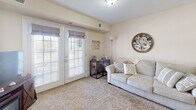 This single-floor residence is thoughtfully designed for comfortable, everyday living. The open-concept layout seamlessly connects the kitchen, dining, and living areas, creating a cohesive and functional space bathed in warm, natural light. The kitchen is well-equipped with honey-toned oak cabinetry, granite-look countertops, and a full suite of white appliances including a range, dishwasher, and refrigerator. A pendant light fixture above the dining area adds a welcoming touch, while durable hardwood flooring runs throughout the kitchen and dining spaces. Adjacent to the kitchen, the living area transitions into a carpeted sitting room featuring large French doors that provide abundant natural light and direct access to the outdoors. The bedroom is a peaceful retreat with soft carpeting, a generously sized window with blinds, and ample wall space. The bathroom is notably spacious, featuring dual vanities with oak cabinetry, well-lit mirrors, and hardwood flooring, offering both functionality and comfort. Throughout the residence, neutral wall tones and consistent finishes create a cohesive, calm ambiance that is both practical and inviting.