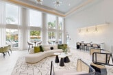 Located at 140 SW 91st Ave in Plantation, Florida, this single-floor amenity space delivers a refined, contemporary aesthetic across a generously sized open-plan layout. Soaring double-height ceilings with recessed tray detailing and gold accent trim establish an immediate sense of grandeur, while dramatic floor-to-ceiling windows dressed in sheer white curtains flood the interior with abundant natural light and frame lush tropical pool views beyond.

Large-format porcelain tile flooring in a white Calacatta marble pattern flows seamlessly throughout, reinforcing the space's clean, upscale character. The main lounge area is anchored by a curved ivory sofa, sculptural coffee tables, and a geometric patterned area rug, complemented by mixed seating including rattan-accented chairs. Striking sputnik-style chandeliers serve as bold focal points overhead.

A built-in wet bar area features navy cabinetry with brass hardware, herringbone mosaic tile backsplash, and pendant lighting, paired with café-style round table seating. A bar-height marble counter with cane-back stools provides additional seating. The leasing or reception area includes a functional workstation desk, wall art, and a bench, maintaining the space's polished, hospitality-inspired atmosphere throughout.