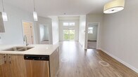 Located at 5477 200 Street in Langley, BC, this well-appointed 2-bedroom, 1-bathroom unit offers a thoughtfully designed layout across a single floor. The open-concept living and kitchen area forms the heart of the home, featuring warm hardwood-style flooring, soft neutral tones, and a pendant-lit kitchen island with a clean white countertop. The kitchen is equipped with stainless steel appliances — including a full-size refrigerator, stove, and microwave — complemented by wood-tone cabinetry and track lighting that adds a modern touch. A dedicated dining or living area flows naturally from the kitchen, bathed in ambient light. Both bedrooms are carpeted for comfort and feature large windows that frame pleasant views of surrounding trees, creating a calm, nature-connected atmosphere. Each room includes closet storage, with the primary bedroom offering generous proportions. The full bathroom is cleanly finished with a soaker tub and shower combination, tiled surround with a tasteful accent detail, and a wide vanity mirror. A dedicated in-unit laundry area with a stacked washer and dryer adds everyday convenience. Neutral wall tones and consistent finishes throughout lend the space a cohesive, move-in-ready appeal.