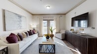 Located at 3871 Redwine Rd in Atlanta, GA, this single-floor residence offers a thoughtfully designed open-concept layout that seamlessly connects its key living spaces. The kitchen is equipped with rich dark cabinetry, black appliances, a deep sink, tile backsplash, and a breakfast bar with pendant lighting, opening directly to the dining area. The dedicated dining space features crown molding, wood-look flooring, and a classic round table setting beneath an elegant overhead light fixture. The living room is bright and welcoming, with large windows and glass doors that invite generous natural light and outdoor views, complemented by crown molding and wood-look flooring that flows throughout the main areas. Two well-sized bedrooms offer carpeted floors, ample natural light through slatted windows, and a calm, neutral palette. The bathrooms feature tile flooring and tub-shower combinations. A hallway with clean white walls and panel doors connects the private areas of the residence. The overall aesthetic is contemporary and cohesive, with warm tones, consistent finishes, and a layout that balances comfort and functionality throughout.