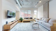 Located at 951 Fell St in Baltimore, MD, this urban loft showcases a striking blend of industrial and contemporary design across a single floor. The expansive living area commands attention with soaring exposed concrete ceilings, visible ductwork, and track lighting that emphasize the space's loft-style character. Large windows flood the room with natural light while offering views of the surrounding neighborhood, complementing the warm hardwood flooring beneath. Exposed concrete columns punctuate the living space, adding to the raw, architectural aesthetic.

The kitchen is well-appointed with warm wood cabinetry, dark granite countertops, stainless steel appliances, and hardwood flooring that continues seamlessly from the living area. An arched architectural detail adds a subtle decorative touch.

The bedrooms maintain the industrial aesthetic with exposed concrete ceilings and generous windows. One bedroom features a spacious walk-in closet with extensive shelving. The bathroom is finished with slate tile flooring, rich wood cabinetry, dark granite countertops, and a tiled tub-shower combination, delivering a polished, upscale feel. Throughout, the space balances raw urban elements with refined modern touches.